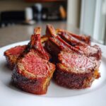 Close-up of perfectly cooked, medium-rare smoked rack of lamb chops served on a white plate.