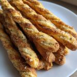 A close-up pile of golden, twisted sourdough discard breadsticks seasoned with herbs and Parmesan cheese.