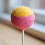 Close-up of a colorful, two-toned starbucks cake pop, half pink and half yellow, coated in sprinkles.
