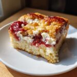 A close-up of a square slice of strawberry cheesecake dump cake showing layers of cake, cream cheese, and strawberry filling.
