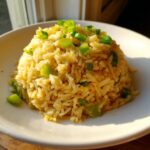 A mound of golden texas roadhouse seasoned rice topped with bright green chopped scallions on a white plate.