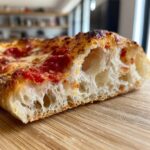 Close-up of a slice showing the airy, open crumb structure of the thick-crust pizza dough topped with sauce and cheese.