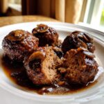 Four rich venison meatballs with Marsala sauce and sliced mushrooms, one cut open to show the texture.