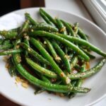 Close-up of bright green, glossy worcestershire sauteed green beans tossed with minced garlic in a white bowl.
