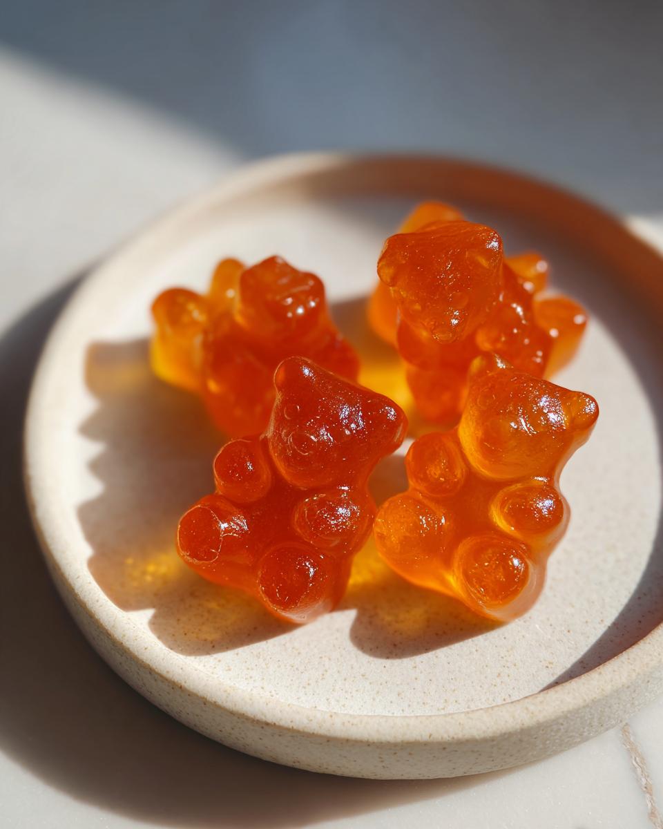 Four translucent, orange apple cider vinegar gummies shaped like bears resting on a small, speckled ceramic dish.