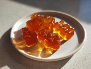 Close-up of several translucent, amber-colored apple cider vinegar gummies shaped like bears on a small white plate.