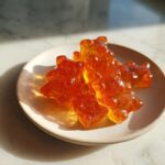 Close-up of several translucent, amber-colored apple cider vinegar gummies shaped like bears on a small ceramic dish.