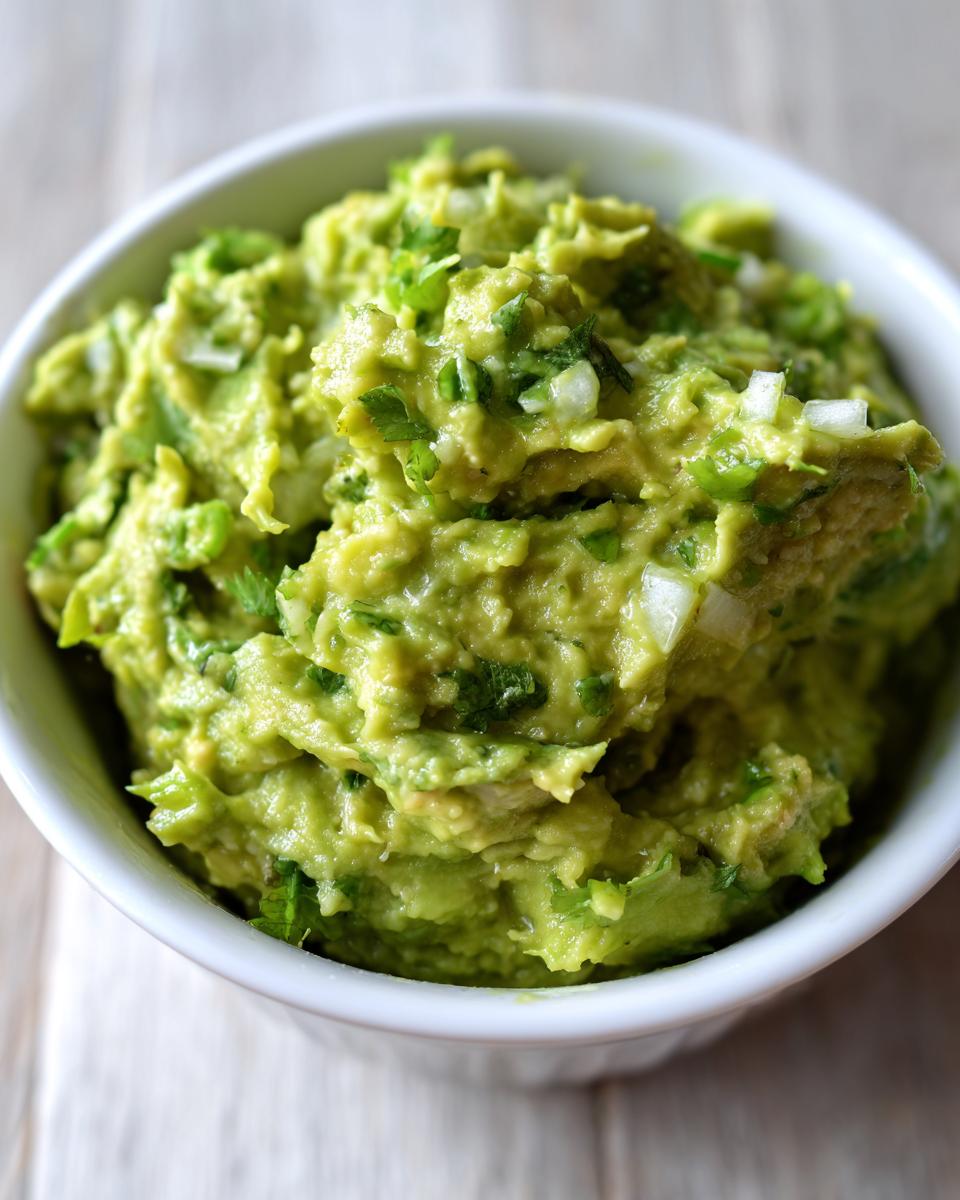 Close-up of a white bowl filled with chunky, vibrant green Authentic guacamole mixed with chopped onion and cilantro.