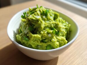 A close-up of chunky, bright green Authentic guacamole topped with chopped onion and cilantro in a white bowl.