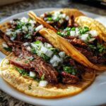 Three delicious Carne asada street tacos served on corn tortillas, topped with diced white onions and fresh cilantro.