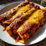 Three rolled chicken enchiladas smothered in red sauce and melted orange and white cheese.