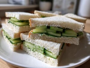 A stack of delicate, crustless cucumber tea sandwiches filled with thinly sliced cucumbers and herbed cream cheese.