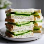 A tall stack of crustless Cucumber tea sandwiches filled with thinly sliced cucumbers on white bread.