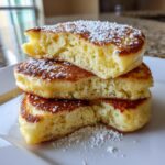 Close-up of a stack of three fluffy Lemon ricotta pancakes dusted with powdered sugar.