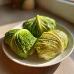 Three bright green cabbage dumplings wrapped in steamed cabbage leaves resting on a light plate.