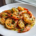 Close-up of juicy garlic butter shrimp coated in herbs and sauce, served in a white bowl.