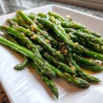 Close-up of bright green Lemon garlic roasted asparagus spears glistening with oil and topped with minced garlic.