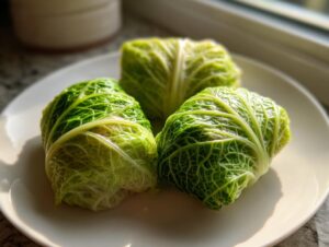 Three bright green cabbage dumplings wrapped tightly in savoy cabbage leaves, resting on a white plate.