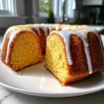 A slice cut from a bundt-style Orange Juice Cake, drizzled with white icing and topped with orange zest.