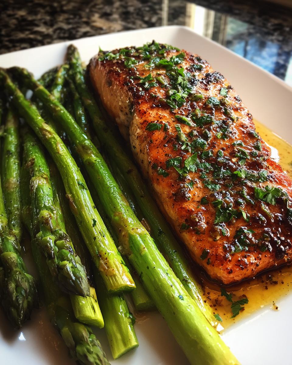 A close-up of a perfectly cooked fillet of Sheet pan garlic butter salmon served alongside bright green roasted asparagus.