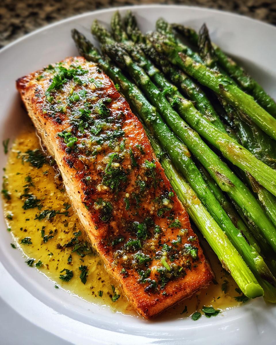 Close-up of a perfectly cooked fillet of Sheet pan garlic butter salmon drizzled with butter sauce, served next to bright green asparagus.