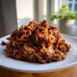 A close-up of a generous mound of perfectly shredded, dark, and caramelized Slow Cooker Pulled Pork Carnitas on a white plate.