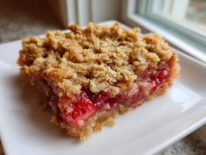 Close-up of a square slice of Strawberry Rhubarb Crisp with a thick, golden oat topping and bright red fruit filling.