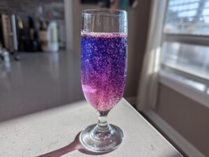 A tall glass filled with bubbly, gradient purple and pink Blueberry lemosas catching the sunlight.