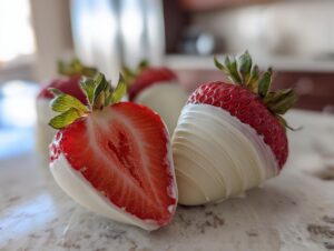 Close-up of fresh strawberries, one whole and one halved, partially dipped in white chocolate, showcasing the vibrant red fruit.