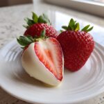 Close-up of white chocolate dipped strawberries, one cut in half showing the bright red interior.